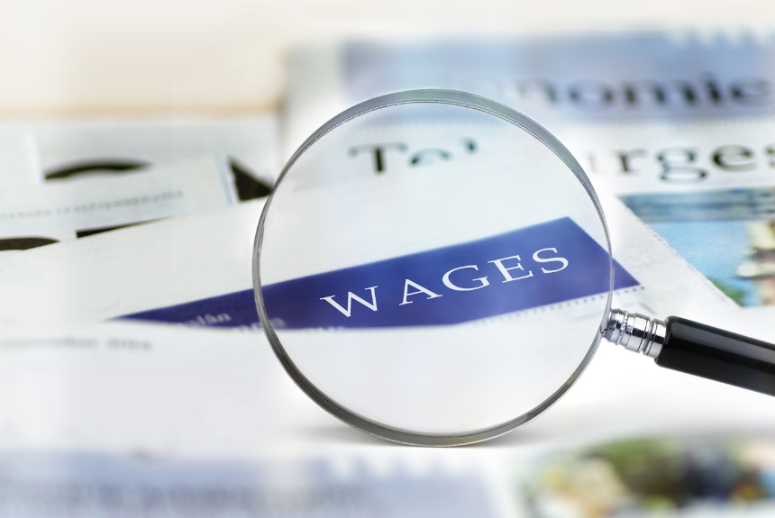 A magnifying glass highlights the word “WAGES” on a newspaper page, symbolizing a focus on salary, income, or financial news.